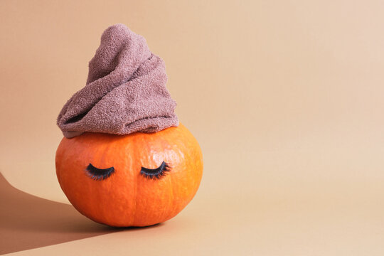 orange pumpkin with towel and false eyelashes on brown background copy space