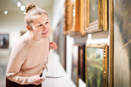 Portrait of young woman with the guide looking at pictures in museum of arts