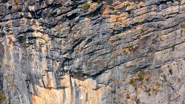 Rough surface and texture of rock on a vertical cliff. Geological layers of earth's crust. Sedimentary strata mountain formation on a rugged canyon wall. Zoom out aerial drone view.