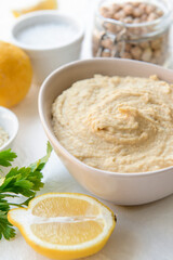 Bowl with tasty hummus and lemon on light background