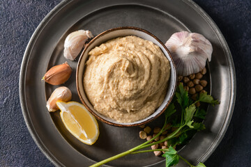 Bowl with tasty hummus and ingredients on dark background