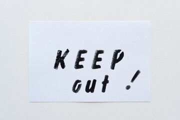 the expression "keep out!" stencilled in black on a white card and placed on a paper background
