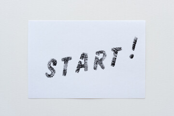 the expression "start!" stencilled in black on a white card and placed on a paper background