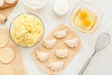 Parchment with raw dumplings and ingredients on light background