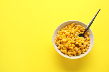 Bowl of corn kernels with spoon on color background