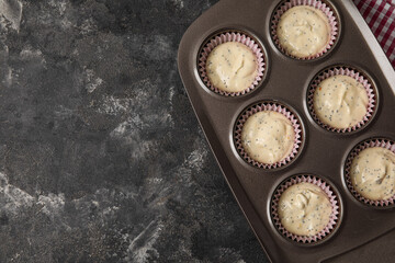 Baking tin with uncooked poppy seed muffins on dark background