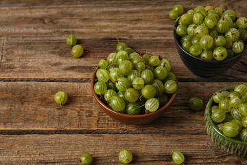 Bowls with fresh ripe gooseberry on wooden background