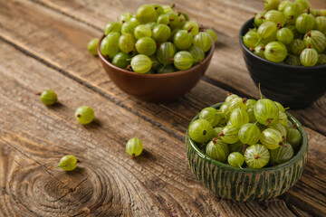 Bowls with fresh ripe gooseberry on wooden background