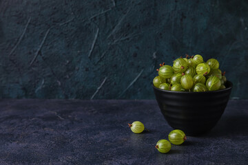 Bowls with fresh ripe gooseberry on dark background