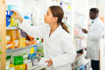 Portrait of a young female pharmacist laying out goods on the shelves of a rack in a pharmacy