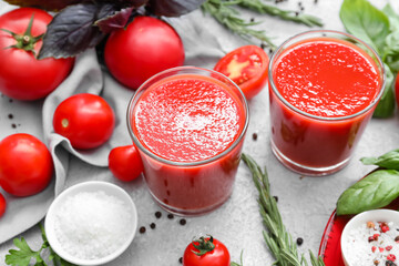 Glasses of tasty tomato juice on light background