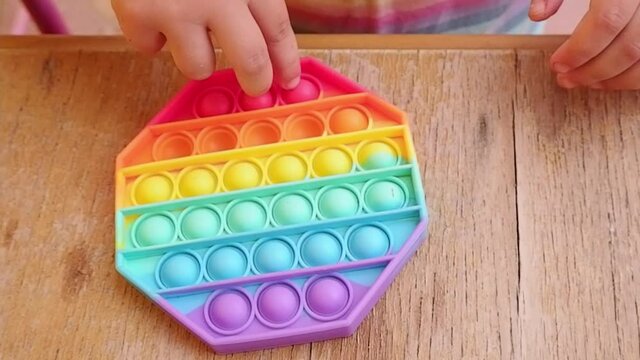 Child playing with pop it silicone toy at wooden table