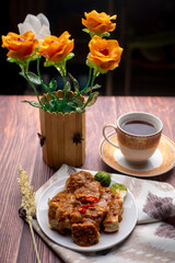 Batagor, Indonesian traditional and street food. Batagor made by fried fish dumpling with fried tofu and served in peanut sauce and served with a cup of tea and lime. Photographed with artificial flow