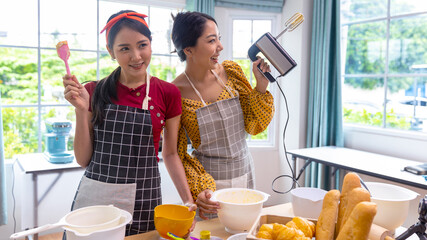 Young female ladies working together in a kitchen for home made bakery business. One lady with apron is teaching a friend on how to make fresh bread at home.