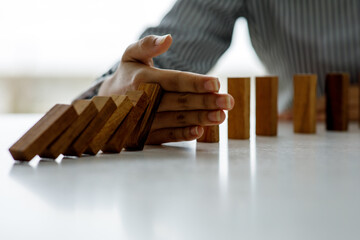 Close up of Hand stopping wooden domino business crisis effect or risk protection concept