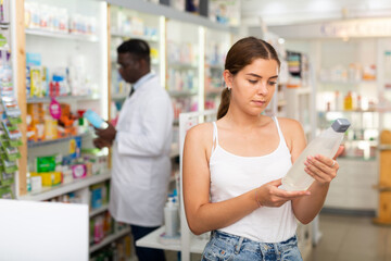 Young woman who came to the pharmacy attentive chooses a hair care remedy, studying its components