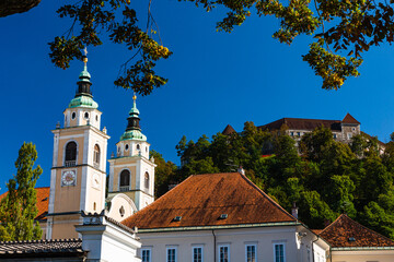 スロベニア　リュブリャナの聖ニコラオス大聖堂と後ろの丘に建つリュブリャナ城 - obrazy, fototapety, plakaty