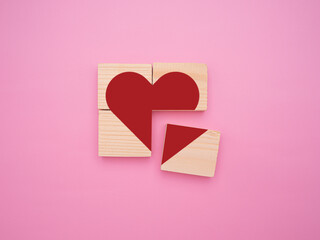 Concept of a broken heart. A red heart symbol on wooden cubes is incomplete on pink background. Top...