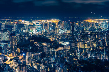 View from above Mori Tower Building in Tokyo illuminated at night with the view of the Rainbow Bridge and Tokyo Airport in the distance in Tokyo, Japan.