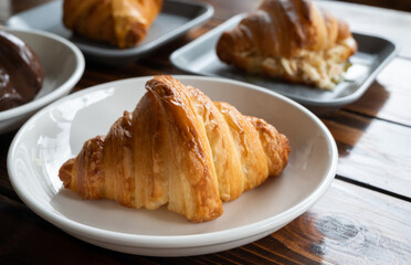 Close up of plain croissants served with plate on wooden table. Croissant is a French buttery, flaky and crescent-shaped bread.