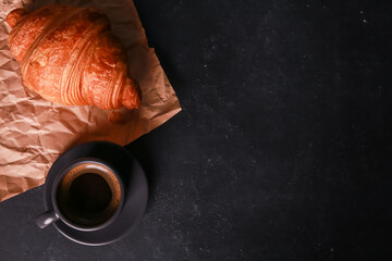 Fresh baked croissant on craft paper, mug of expresso on dark concrete table. Cup of hot coffee,...