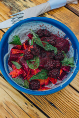 top down shot of a summer salad with red beets, blackberries, mint, carrots, yogurt, and sumac in a blue bowl 
