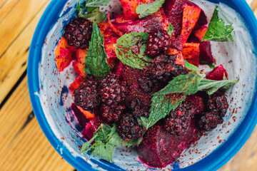 top down shot of a summer salad with red beets, blackberries, mint, carrots, yogurt, and sumac in a blue bowl 