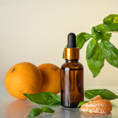Vitamin C serum. Essential oil. A brown glass bottle with a dropper, mandarin slices with basil leaves on a light background. Health and beauty concept. Organic natural cosmetics.