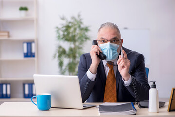 Old male employee working in the office during pandemic