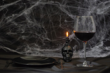 Scary halloween dinner party concept with a glass of red wine, black plate, knife, fork and skull...