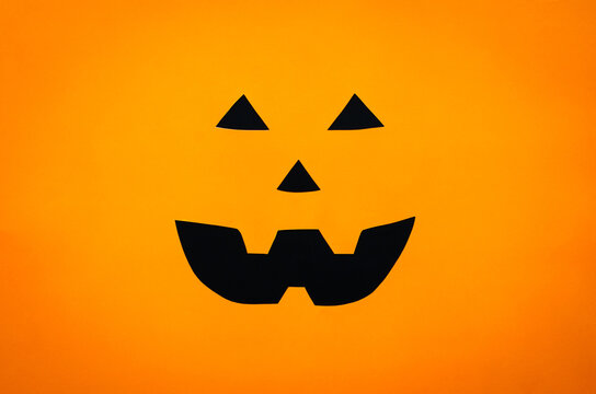 Halloween pumpkin face background from cutting orange and black paper. Minimal halloween concept.