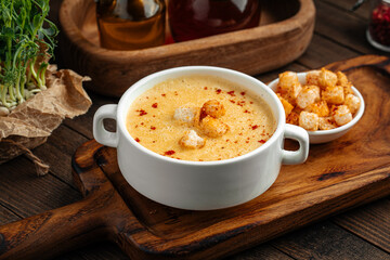 Yellow chicken cream soup with croutons in a white bowl on rustic background