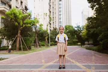 Schoolgirl back to school after summer vacations. Child in uniform smiling early morning outdoor. 
