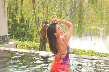 Beautiful Asian woman in colourful swimsuit posing and smiling in the swimmimg pool.