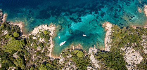 View from above, stunning aerial view of a green and rocky coastline with some boats sailing on a turquoise water. Liscia di vacca,Sardinia, Italy.