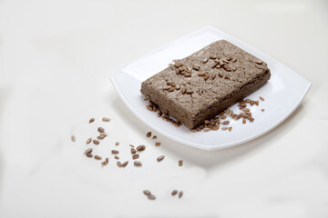 Halva made from sunflower seeds lies on an abelian plate and seeds are scattered nearby on a white background. Copy spaes.
