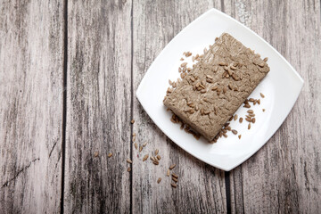 Sunflower seed halva lies on a white porcelain plate on a wooden background.