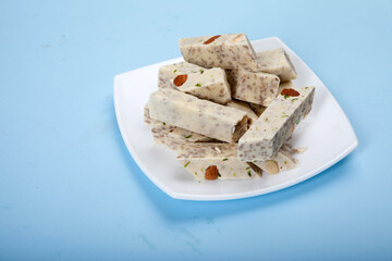 Halva with pistachios and almonds is on a white porcelain plate against a blue background.