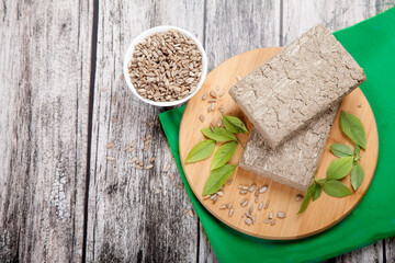 Briquettes of sunflower halva, sunflower seeds and green leaves lie on a wooden board on a green napkin.. A cup of honeycomb sunflower seeds nearby.