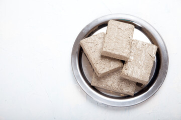 Halva from sunflower seeds in briquettes in a metal plate stands on a white background. Copy spaes.