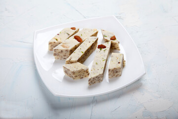 Halva with pistachios and almonds on a white porcelain plate on a white background.
