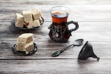 Turetius a glass of tea, a metal spoon and sunflower halva with almonds and pistachios stands on a wooden background.