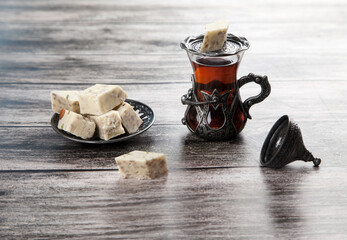 Turkish glass with tea and halva on a metal plate stand on a wooden background.