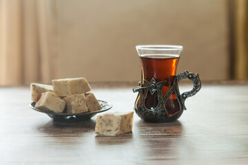 Turkish glass with tea and halva on a metal plate stand on a light background.