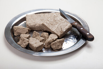 Briquettes and pieces of sunflower halva and a knife lie on a metal grater on a white background.