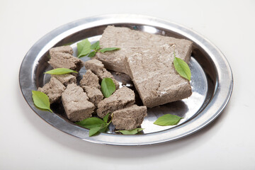 Briquettes and pieces of halva and green basil leaves lie on a metal plate on a white background.
