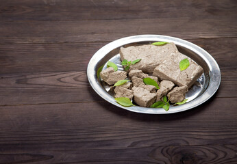 Briquettes and pieces of halva and green basil leaves lie on a metal plate on a wooden background. Copy spaes.