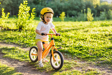 Little cute adorable caucasian toddler girl having fun riding exercise balance run bike push scooter in park forest. 