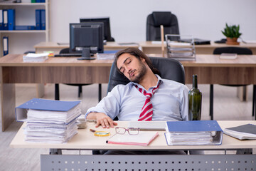 Young male employee drinking alcohol in the office