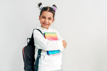 Horizontal view of happy little girl with backpack smiling looking at camera carrying some...